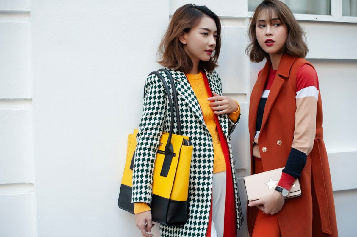 Offres Two fashionable women in vibrant winter attire posing outdoors, showcasing chic handbags and coats.