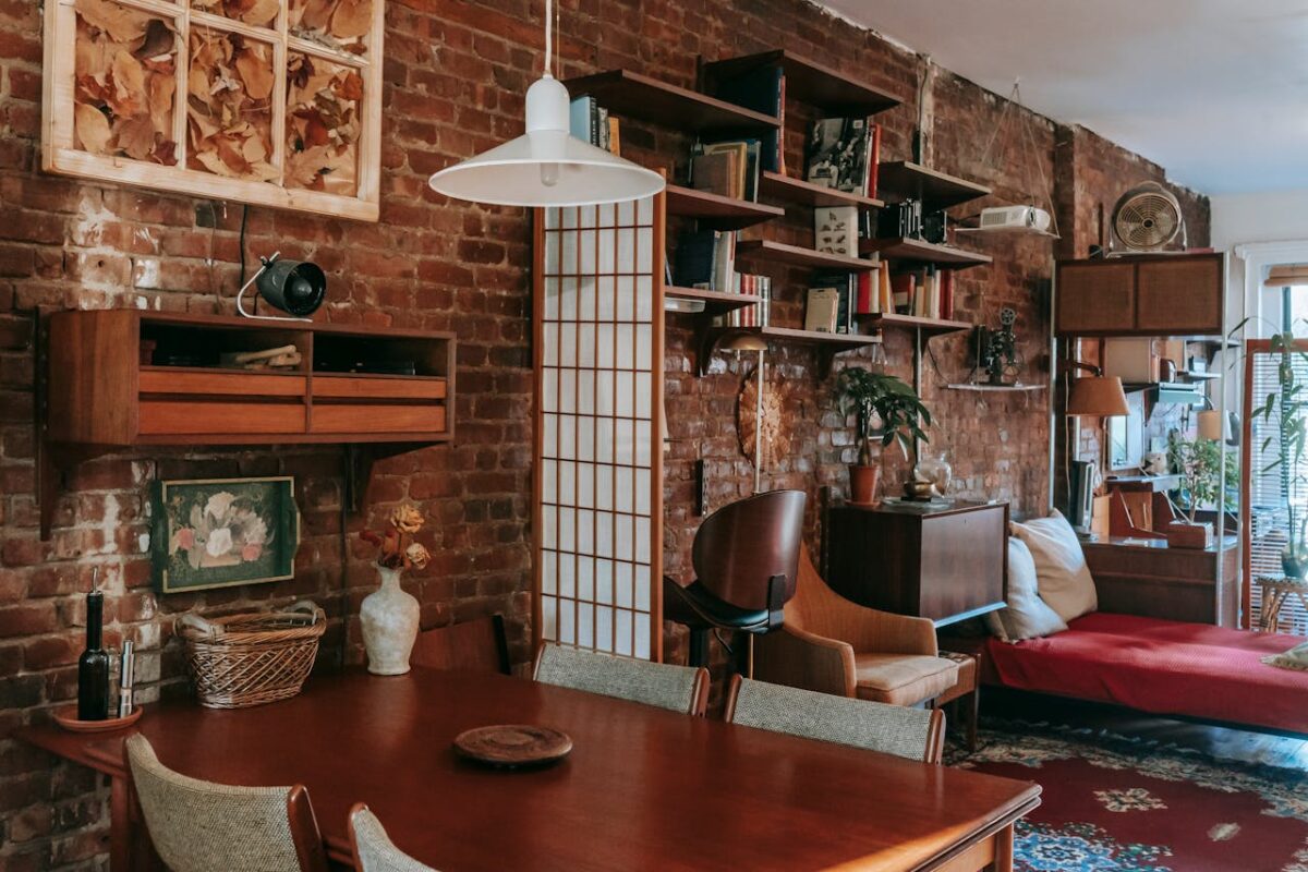 À propos Interior of cozy vintage styled dining room with classic wooden table and chairs placed near weathered brick wall decorated with paintings and bookshelves