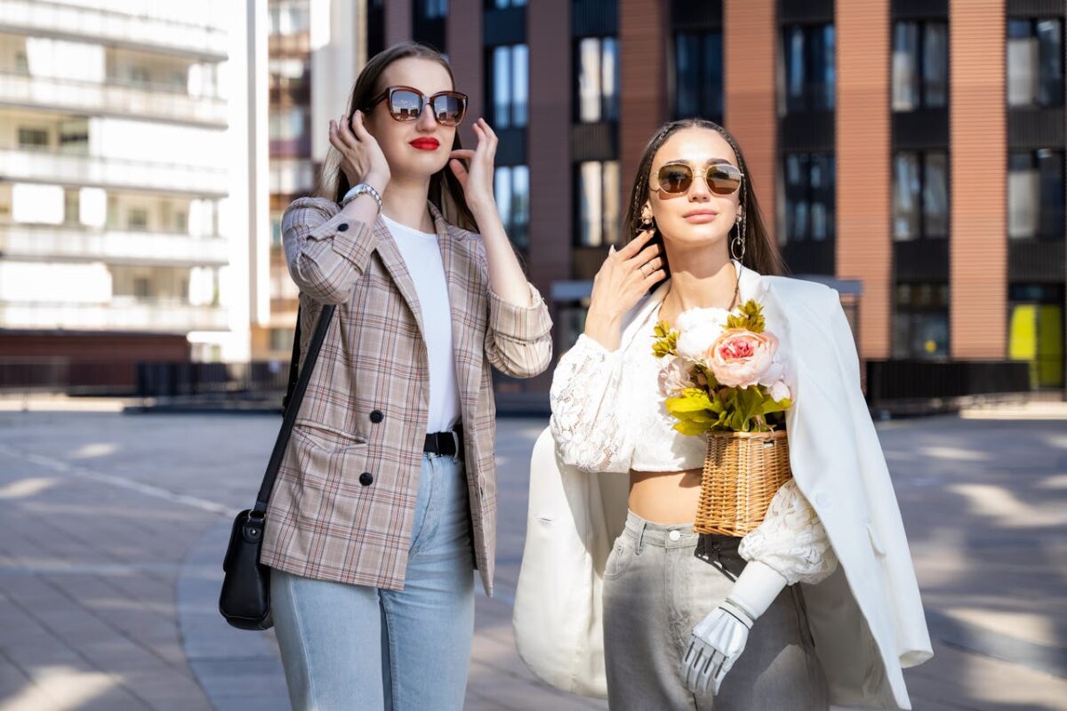 Offres Two stylish women enjoy a sunny day in the city wearing chic outfits and sunglasses.